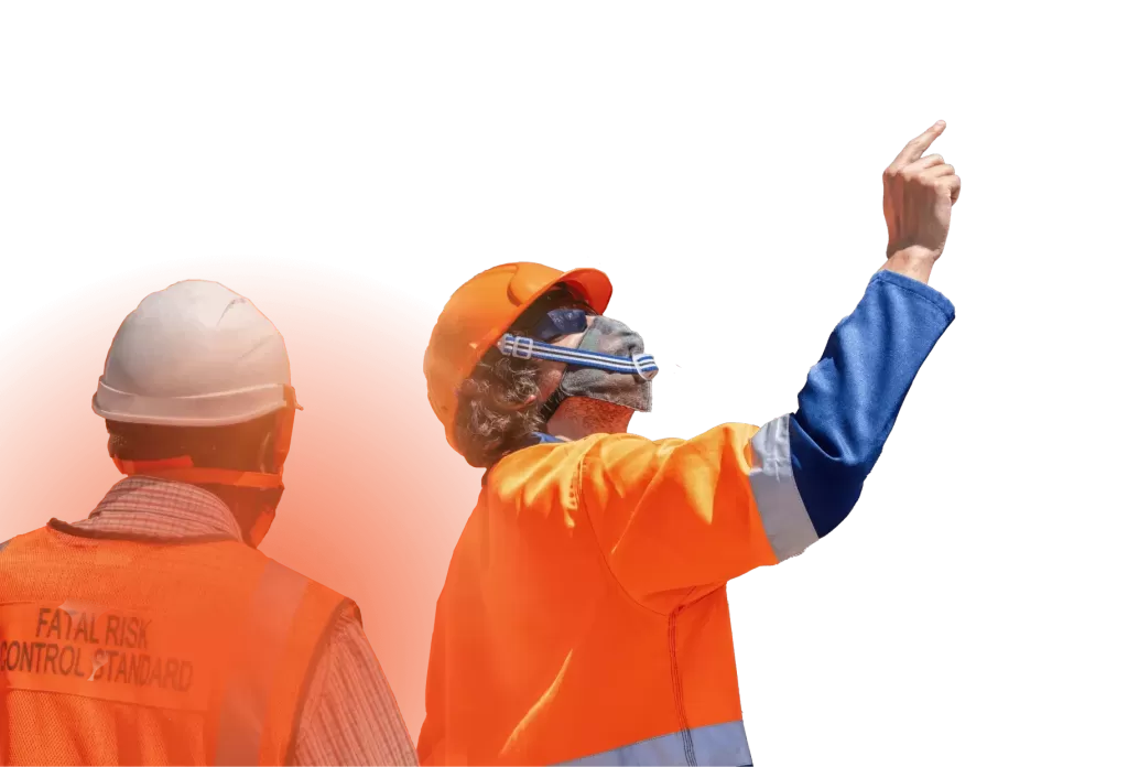 Two construction workers in orange safety vests and helmets, one pointing upwards, appear to be discussing something on a work site.