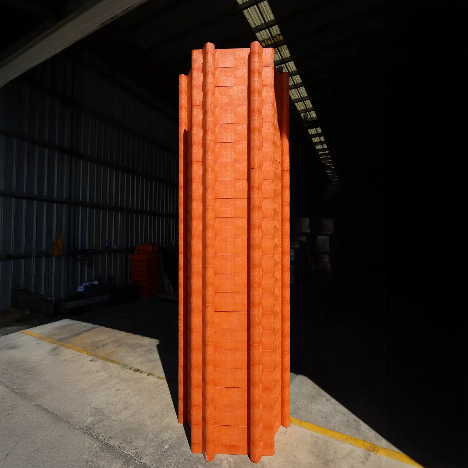 Tall, orange, plastic modular structure stands upright inside a partially lit industrial warehouse with concrete floor and metal walls.